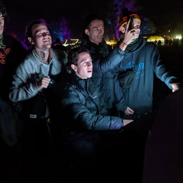 Three participants watching and pointing towards an illuminated installation at night.