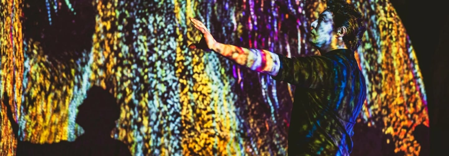 Participant reaching towards a wall of colourful vertical projected light.