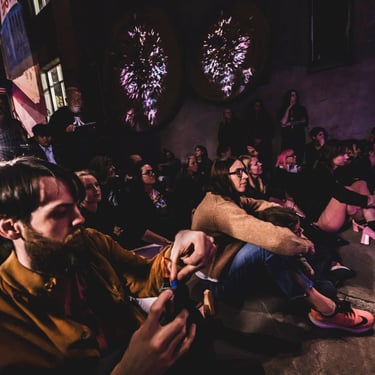 Audience gathered beneath an installation of illuminated sculptural forms at night.