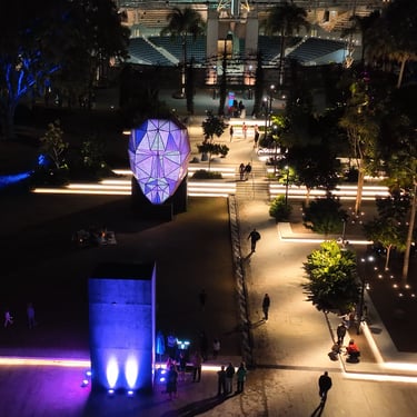 Elevated view of visitors moving through an outdoor installation with illuminated head-shaped sculptures.
