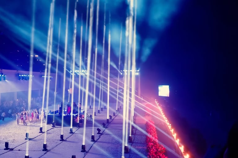 Tall illuminated columns and sweeping coloured light patterns at an outdoor event at night.