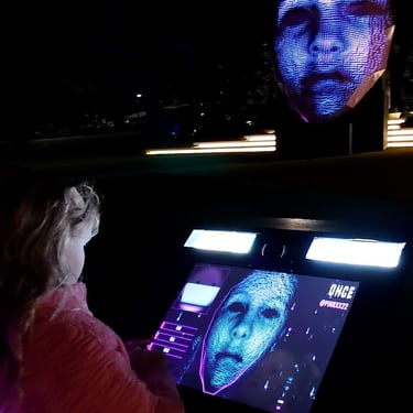 Participant using a touchscreen showing a face, with an illuminated head sculpture beyond.
