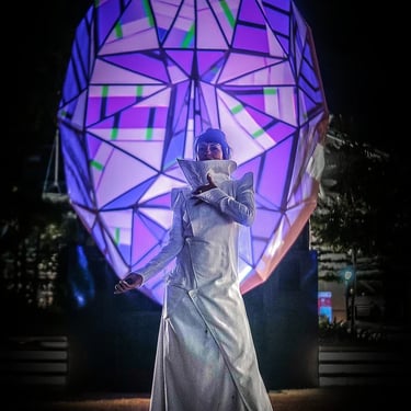 Visitor standing beneath a large faceted illuminated head displaying purple and blue geometric patterns.