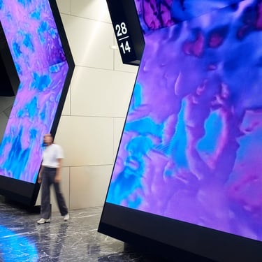Visitors beside tall projection panels displaying purple and blue water-like forms.