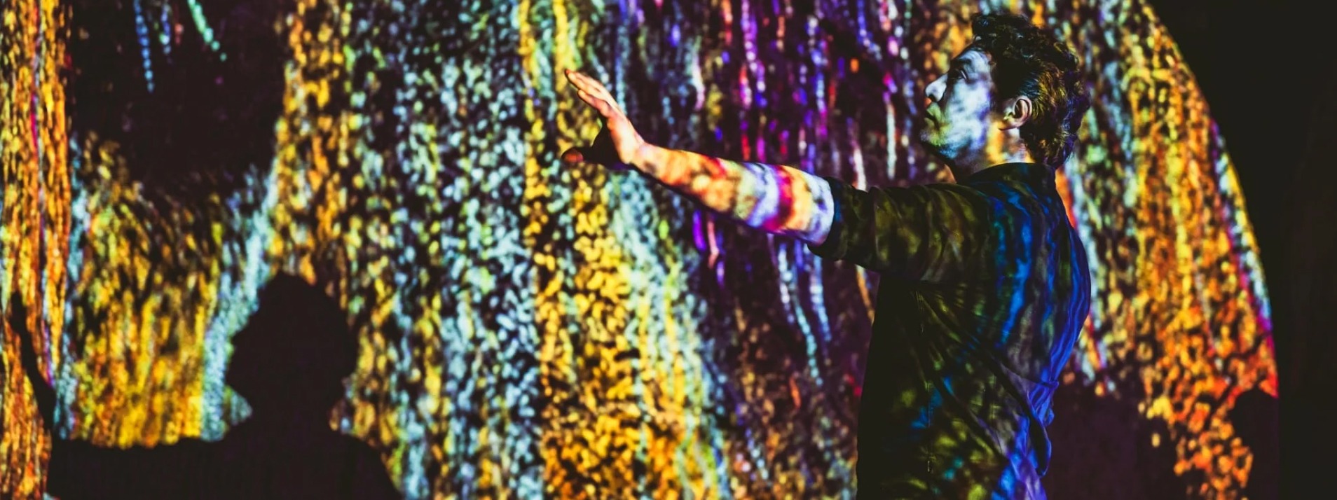 Participant reaching towards a wall of colourful vertical projected light.