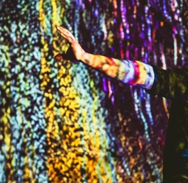 Participant reaching towards a wall of colourful vertical projected light.