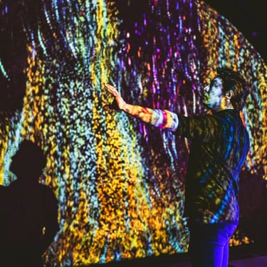 Participant reaching towards a wall of colourful vertical projected light.