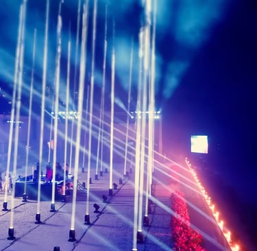 Tall illuminated columns and sweeping coloured light patterns at an outdoor event at night.