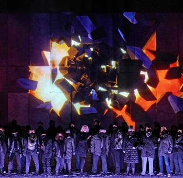 Performers on stage beneath angular purple, orange and white projections.