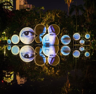 Projected eyes and faces arranged across circular screens in a garden at night.