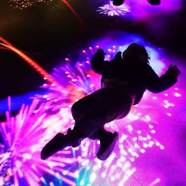 Silhouetted participant jumping above a magenta and blue illuminated interactive floor.